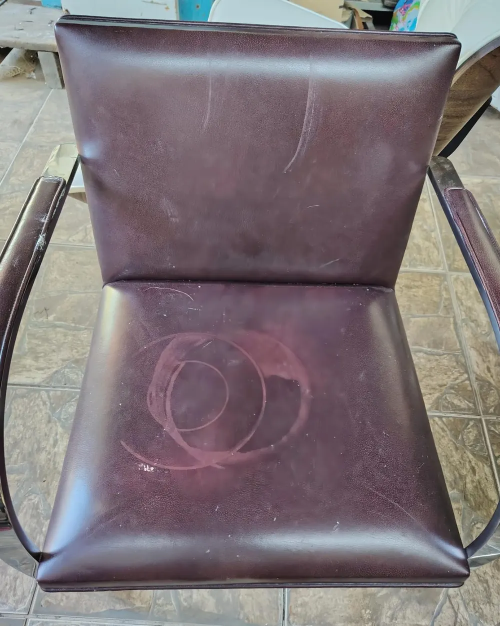 Poltrona de couro bordô com mancha circular no assento e riscos no encosto