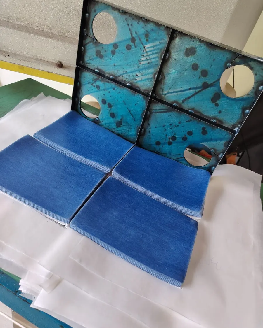 Faca de corte em balancim apoiada sobre as peças de jeans já cortadas